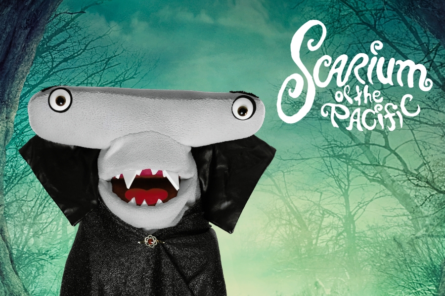 Seymour the hammerhead shark puppet wearing a vampire costume with the text/logo "Scarium of the Pacific" floating eerily above. The background features a sickly green hazy sky and dark barren tree branch silhouettes.