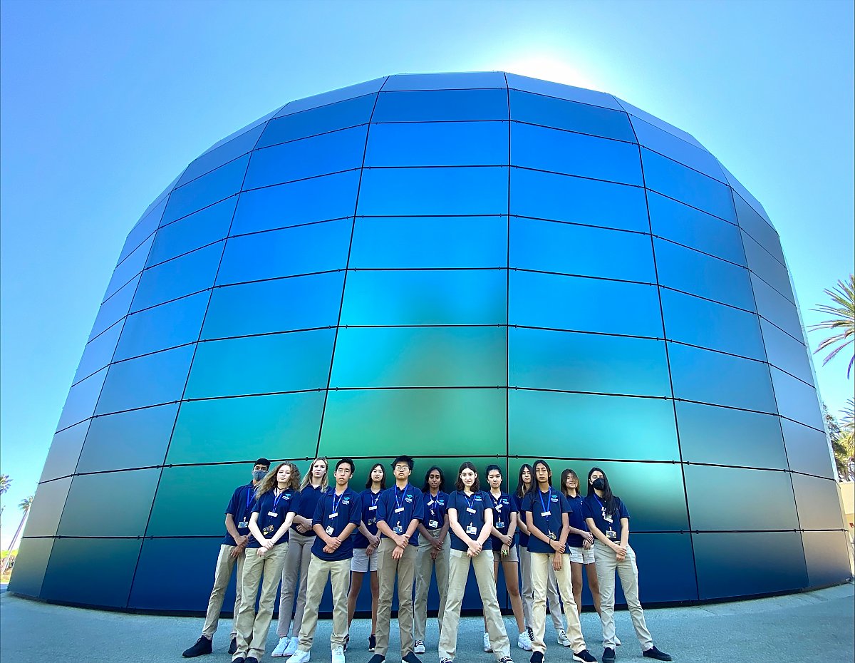 Group of teen volunteers pose in front of the Pacific Visions building with sun behind