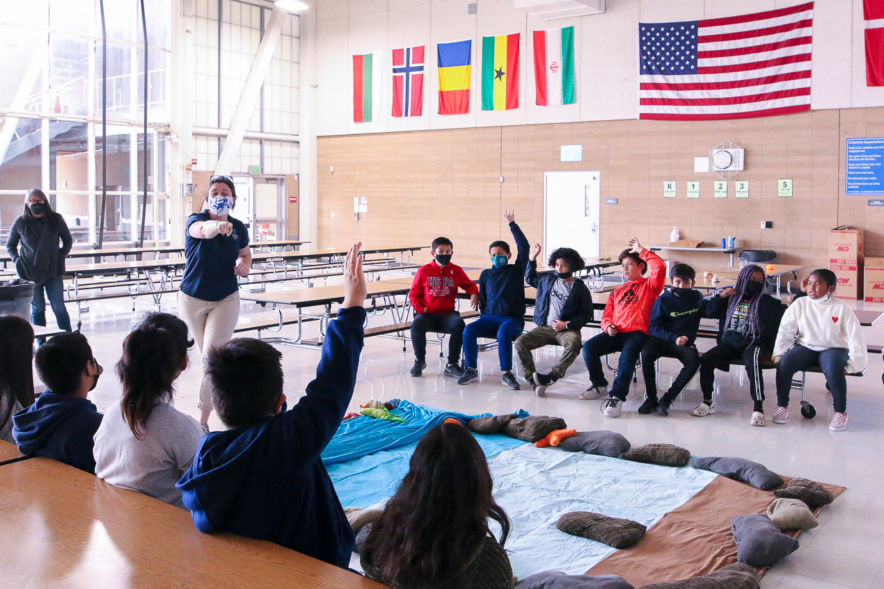 Classroom with kids raising hands and teacher pointing