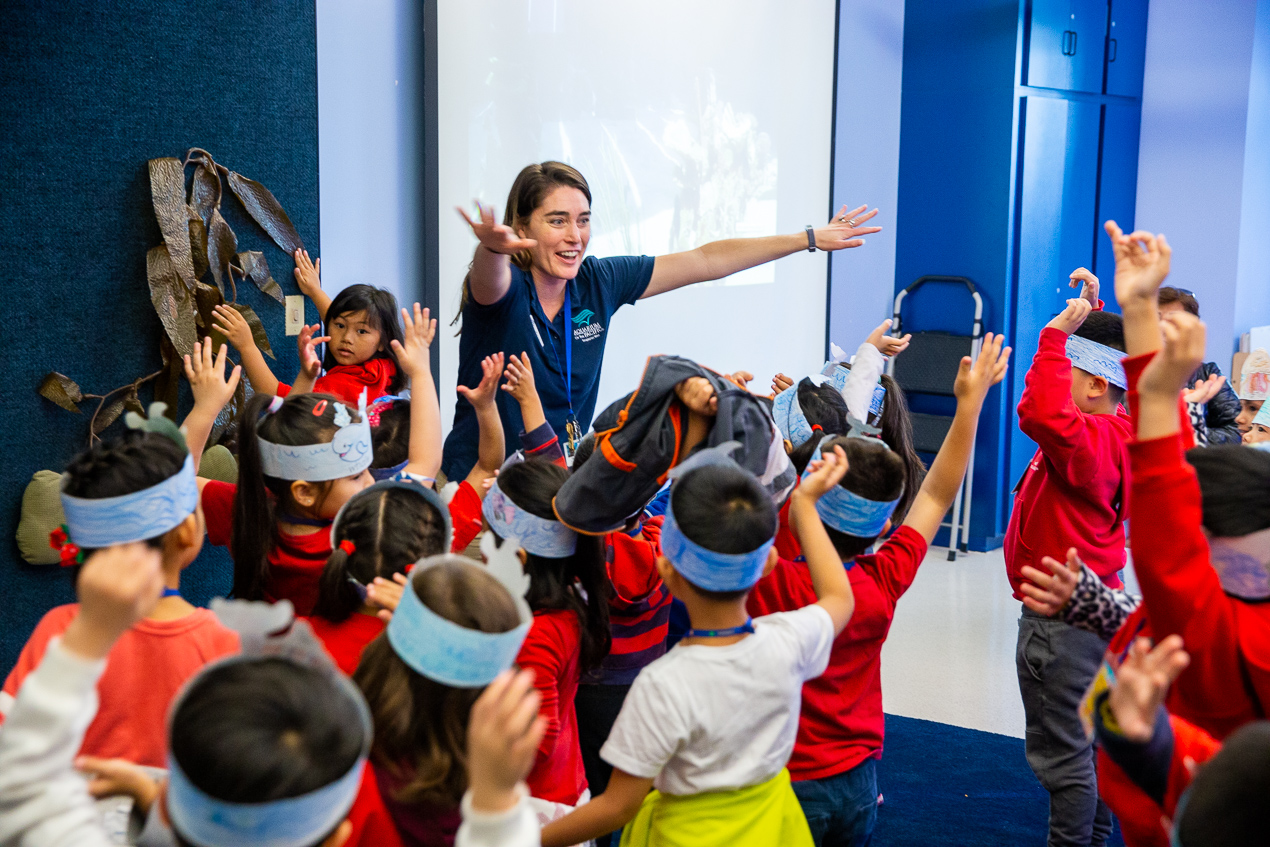 Educator and kids in class holding up hands